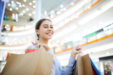 Büyük modern çarşıda alışveriş yaparken kameraya bakarak paperbags olan güzel kadın
