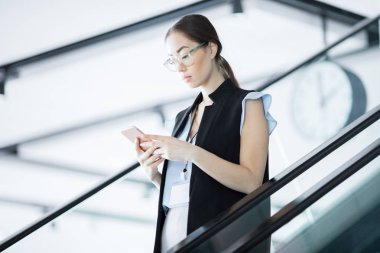 Yürüyen merdivenüzerinde hareket ederken akıllı telefonda konferans okuma mesajı meşgul genç katılımcı