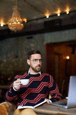Genç adam kafeteryada otururken bilgisayarından internetten bir şeyler izliyor.