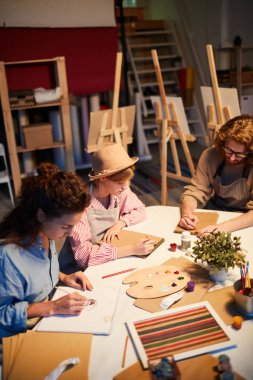 Bireysel çalışma sırasında masaya oturan ve not defterlerinde çizim yapan küçük öğrenci grubu