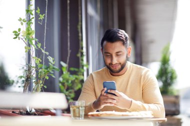 Kafede öğle yemeği ile servis masa tarafından otururken akıllı telefon mesajlaşma veya okuma mesajı ile Çağdaş adam