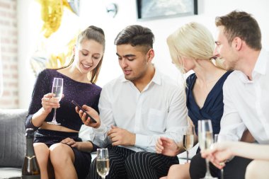 Şampanya ile iki kız ve adam partide meraklı bir şey izlemek için arkadaşlarının akıllı telefon bakarak