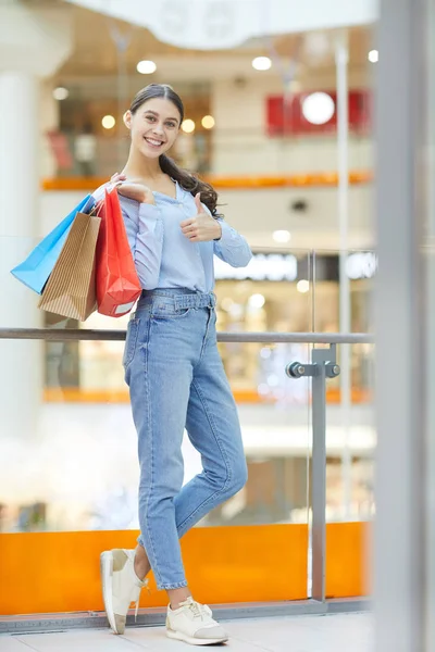 快乐的年轻购物者穿着休闲衬衫和蓝色牛仔裤 站在现代大型商场时露出大拇指 — 图库照片