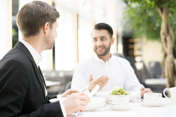 ナイフとフォークを持つビジネスマンがレストランで昼食を食べ ビジネスパートナーに耳を傾ける — ストック写真