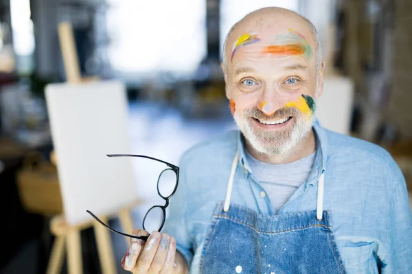 Uśmiechnięty Dojrzały Człowiek Farby Twarzy Trzyma Okulary Patrząc Ciebie — Zdjęcie stockowe