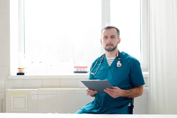 Seriózní Lékař Uniformě Který Sedí Okna Schránkou Během Práce Klinikách — Stock fotografie