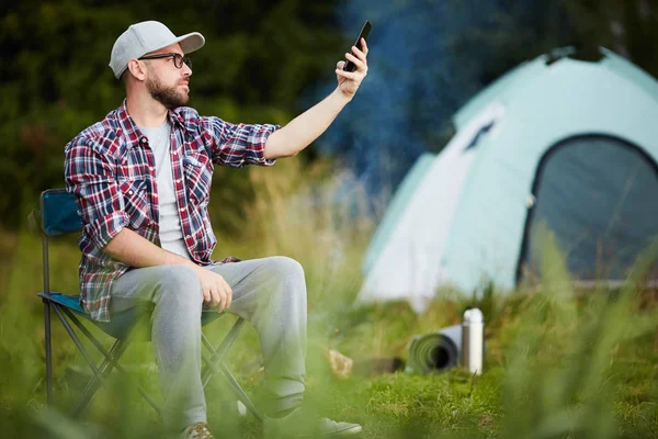 若い男が椅子に座ってキャンプで携帯電話の接続をキャッチします — ストック写真