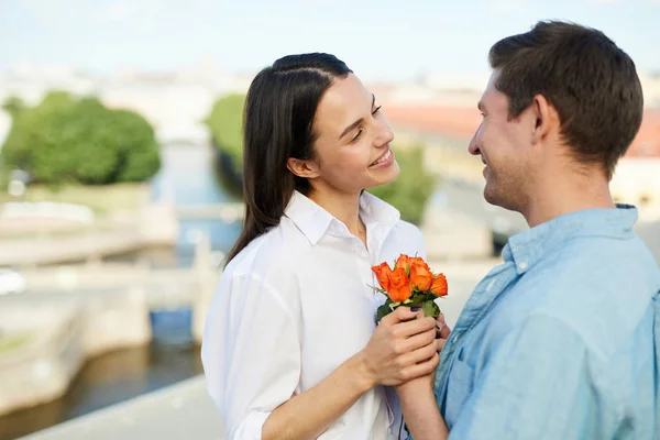 快乐的年轻人衬衫给漂亮的鲜花微笑美丽的女朋友 而他们站在屋顶上 看着眼睛 — 图库照片
