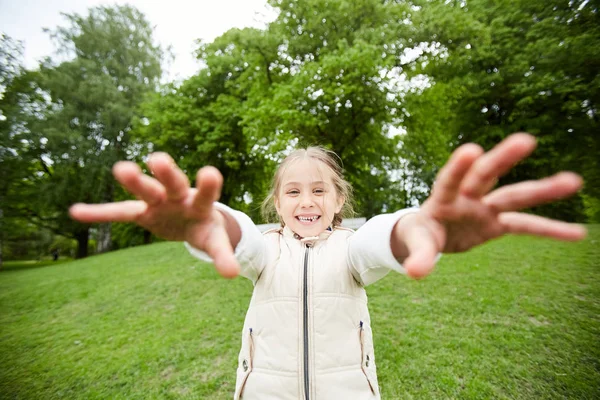 公園の緑の芝生で楽しみながらあなたに彼女の手を伸ばす笑う小さな女の子 — ストック写真