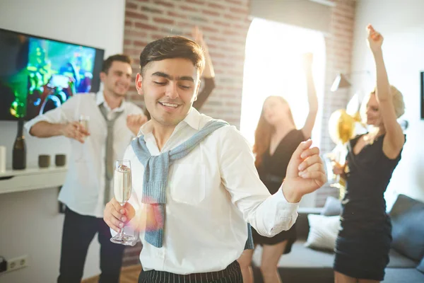 欢快的家伙与香槟长笛跳舞在家里党与他的朋友的背景 — 图库照片