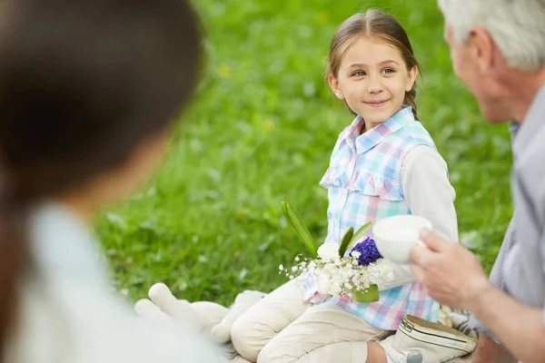 ピクニックでお茶のカップで話している間に祖父を見て花の花束を持つかわいい女の子 — ストック写真