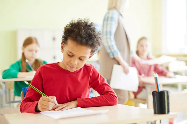赤いセーターを着た自信のあるアフリカ系アメリカ人の男子生徒が机に座り クイズに合格しながら空白で答えをマークする — ストック写真