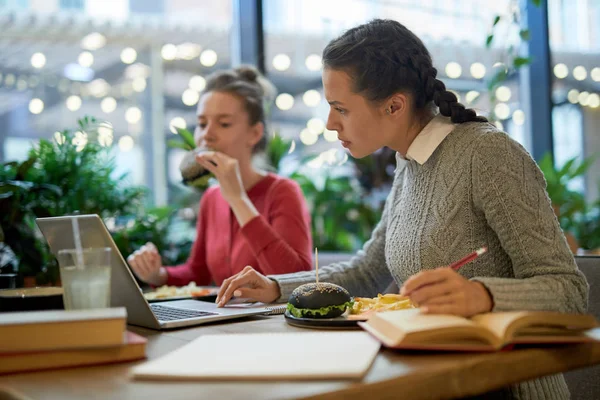 一个女孩在大学咖啡馆吃午饭时准备家庭作业时在网上搜索 — 图库照片