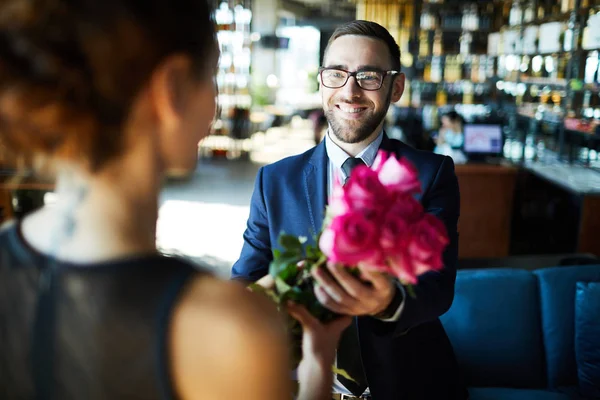 スーツとメガネのレストランで彼のガールフレンドにバラの花束を与えるの幸せな男 — ストック写真