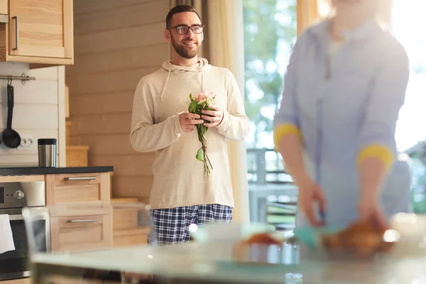 年轻的白种人长胡子的男人站在厨房里 拿着一小束鲜花 准备在妻子做早餐的时候给她一个惊喜 — 图库照片