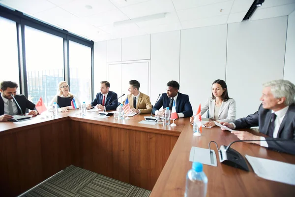 Toplantıda uluslararası tartışmalara katılırken gelecek planları tartışırken formalwear neşeli kendinden emin çok ırklı konsoloslar