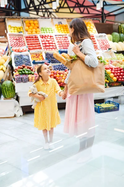 年轻的母亲和漂亮的女儿站在有机食品店里 手牵手聊天 一起购买新鲜食品 — 图库照片