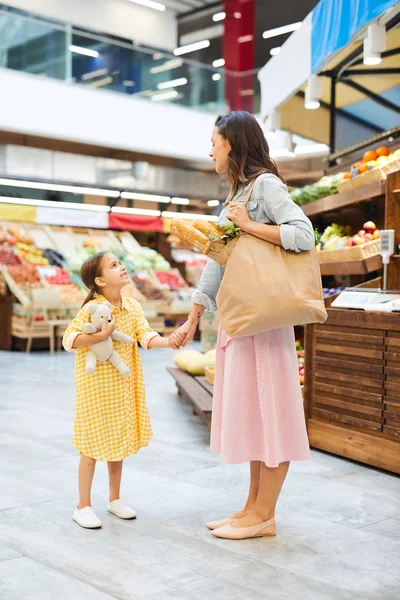 微笑的年轻母亲穿着休闲服装 拿着一袋有机食品 和女儿走过农贸市场 她们聊天 — 图库照片