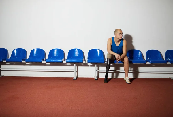 年轻的残疾人 用人造腿坐在椅子上 沿着墙等待轮到他比赛 — 图库照片