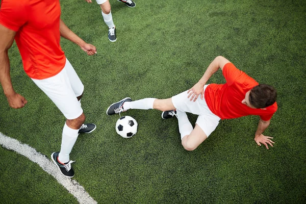 半分近くで彼の仲間とサッカーのフィールドで横になっている時のサッカー ボールをキックするつもりの若いプレーヤーのトップ ビュー — ストック写真