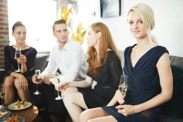 若いですブロンド女性でスマート黒ドレス保持フルートのシャンパンとパーティーを楽しみながら友人 — ストック写真