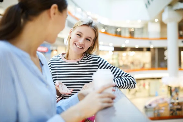 穿着条纹套头衫的快乐女孩在现代商场购物时喝酒时与朋友交谈 — 图库照片