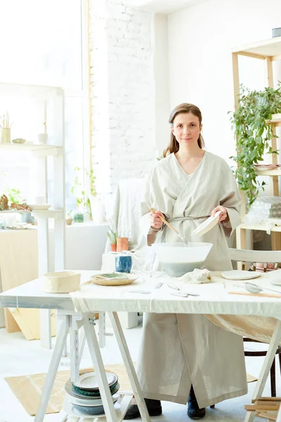 さらに仕事のために特別なプラスチック製のボウルに粘土混合物を作りながら 若い女性はカメラを見て — ストック写真