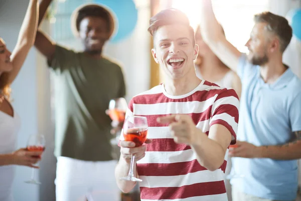 笑的家伙与饮料指向你 而有乐趣在党与跳舞的朋友的背景 — 图库照片