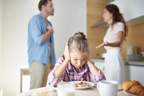 両親のけんかを背景に朝食時にテーブルに寄りかかっている間 耳を覆うストレスを感じた少女 — ストック写真