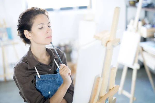 Joven Pintora Pensativa Sosteniendo Lápiz Por Barbilla Mientras Mira Pintura — Foto de Stock