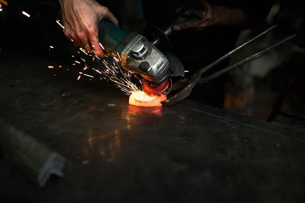 工場のワークスペースでトングによって保持される加熱されたディテールを粉砕認識できない鍛冶屋のクローズアップ — ストック写真
