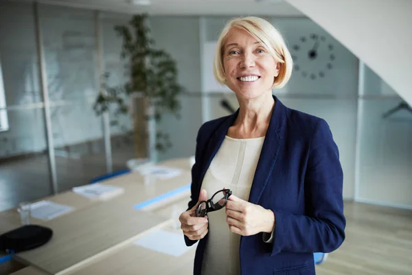 会議室のカメラの前に立つ歯の笑顔とブロンドの髪を持つ成熟したビジネスウーマン — ストック写真