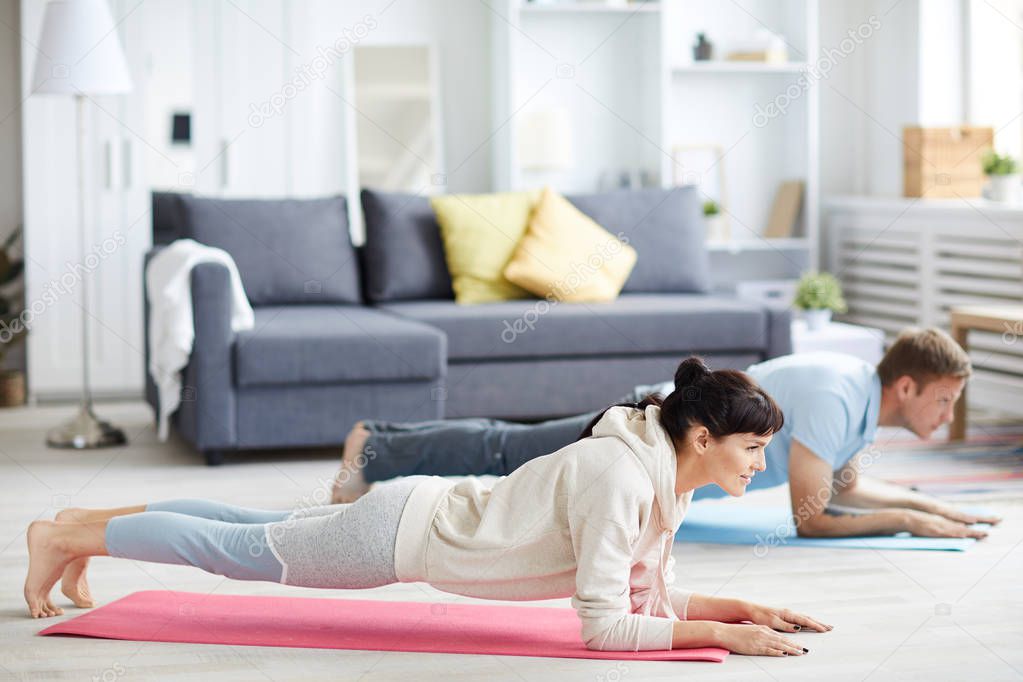 Young man and woman in activewear doing plank during workout at home