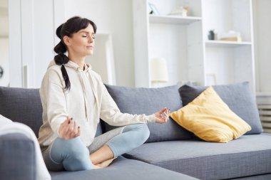 Yoga yaparken gözleri kapalı kanepede nilüfer çiçeği pozu veren genç bir kadın.
