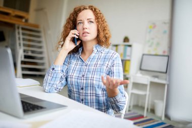 Akıllı telefon dizüstü bilgisayar önünde oturan ve müşterileri telefonla ile Pretty genç ev ofis yöneticisi