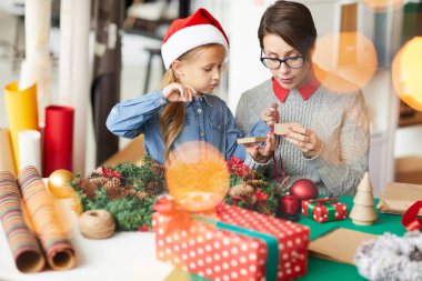 Küçük kızıyla xmas sürprizleri hazırlarken açık hediye kutusuna bakan genç bir kadın.
