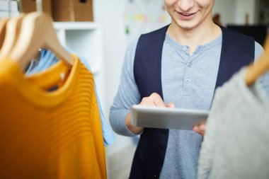 Askıdaki giysiler ve internette arama yapmak arasında duran tabletli bir moda tasarımcısısın.