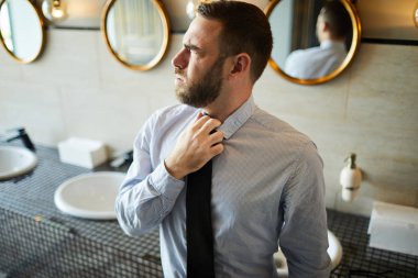 Businessman loosing his tie while visiting lavatory in airport before flight clipart