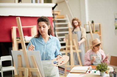 Günümüz sanat atölyesinde gündelik kıyafetlerle resim yapan genç bir kadın.