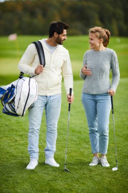 Oynamak için yer tartışan golf kulüpleri ile mutlu genç aktif çift