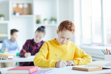 Sarı sweatshirt sevimli kız öğrenci masa başında oturan ve derste copybook notlar yapma