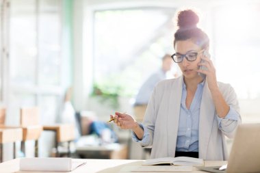 Meşgul genç zarif uzman akıllı telefon ve çözüm organizasyonu veya işyeri tarafından çalışma noktaları ile konuşma