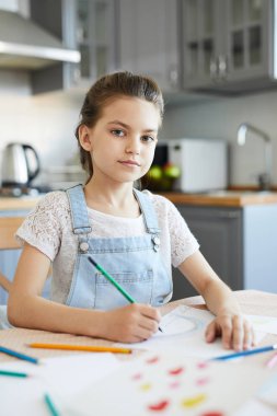 Hafta sonu evde boya kalemleriyle çizim yaparken sana bakan sıradan giyimli güzel küçük kız