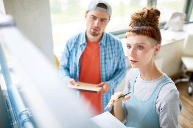 Sınıfta tahtada bekleyen, notlara bakan ve seminer veya projeye hazırlanan iki genç öğrenci