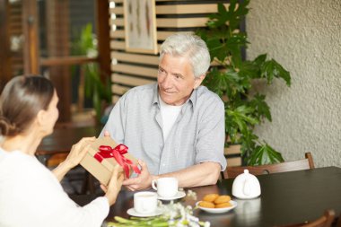 Hem kafede otururken Doğum günü hediyesi ile kutu veren yaşlı gri saçlı adam