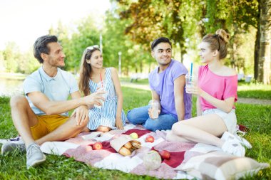 Sıcak yaz gününde parkta boş vakit geçiren içeceklerile mutlu ve samimi gençler