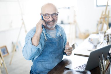 Olgun sakallı adam stüdyo ve ağ masada otururken akıllı telefon ile konuşurken