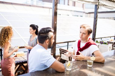 İçkili genç adam açık hava kafeteryasının tezgahında duruyor ve o gün için planlarını tartışıyor.