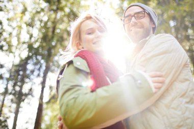 Ormanda birbirlerine sarılırken genç Kafkas çiftin düşük açı görünümü ve güneş parlak parlayan iken kamera mutlu gülümsüyor