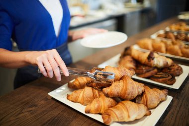 Kafeterya çalışanı bir müşteri için tepsiden taze kabuklu kruvasan birini alarak